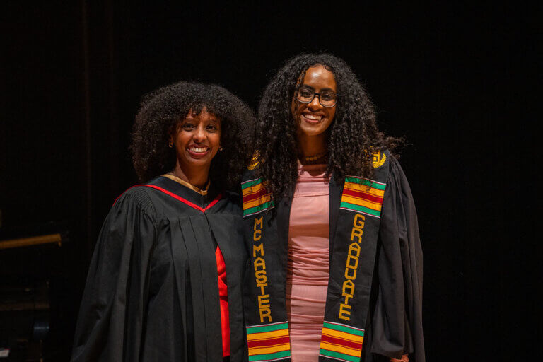 Two female students in graduation attire, smiling together.