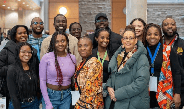 Dr. Clare Warner in green jacket and a group of twelve people posing indoors at MUSC.