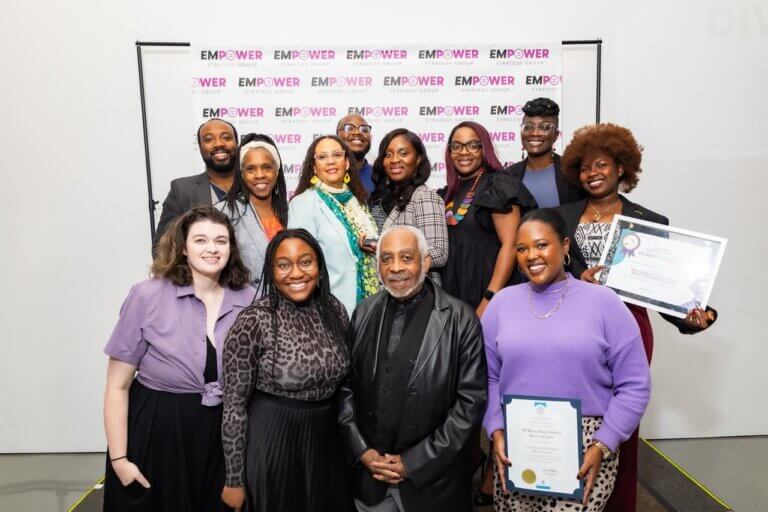 Group of thirteen people posing in front of a backdrop with