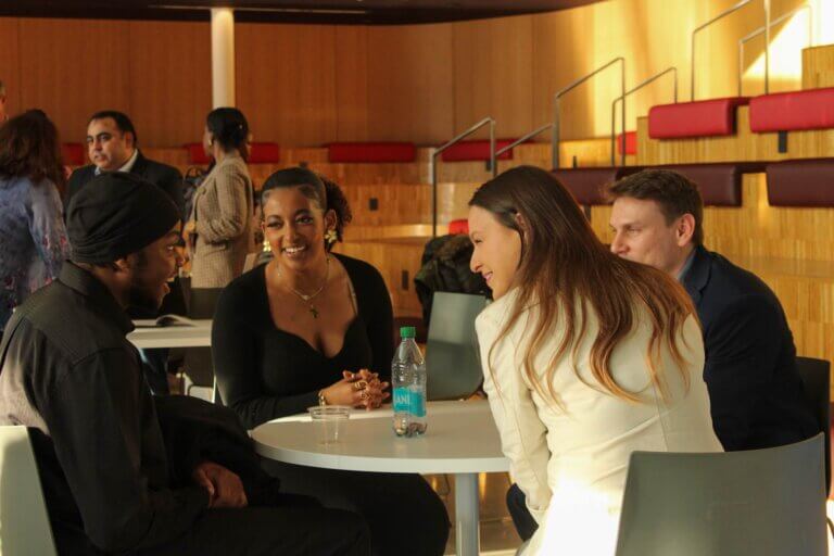 Four people sitting at a round table, engaged in conversation, in a modern indoor setting.