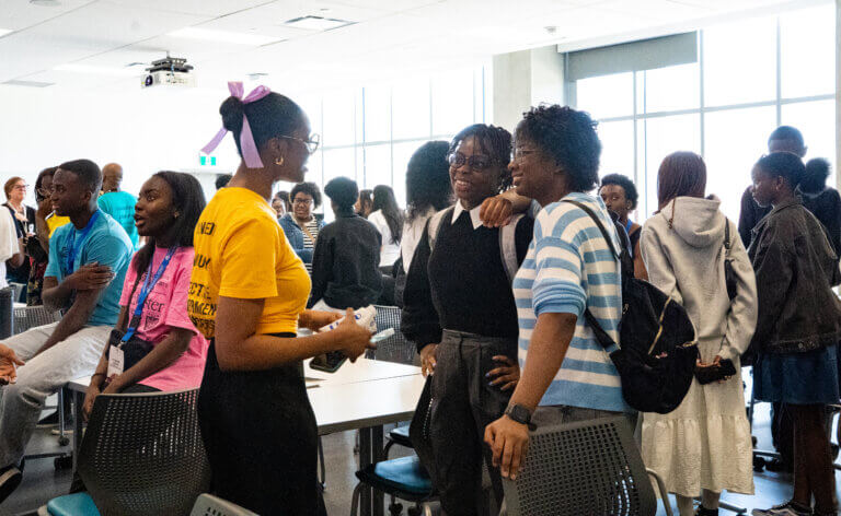 Group of people socializing in a brightly lit room with large windows.