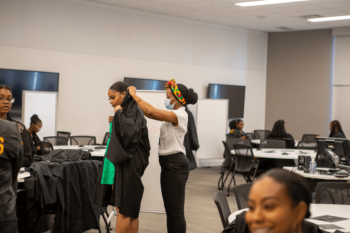 An image containing a graduate being helped put the robe on.