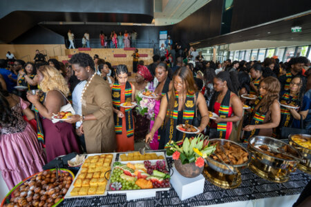 A diverse group of people in colorful attire gather around a buffet table at a joyful event, selecting from a range of vibrant fruits and pastries.